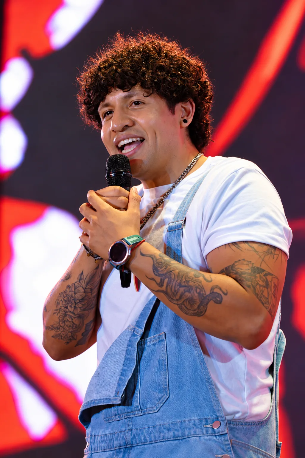 Juan Peralta haciendo stand-up con micrófono frente a pantallas rojas